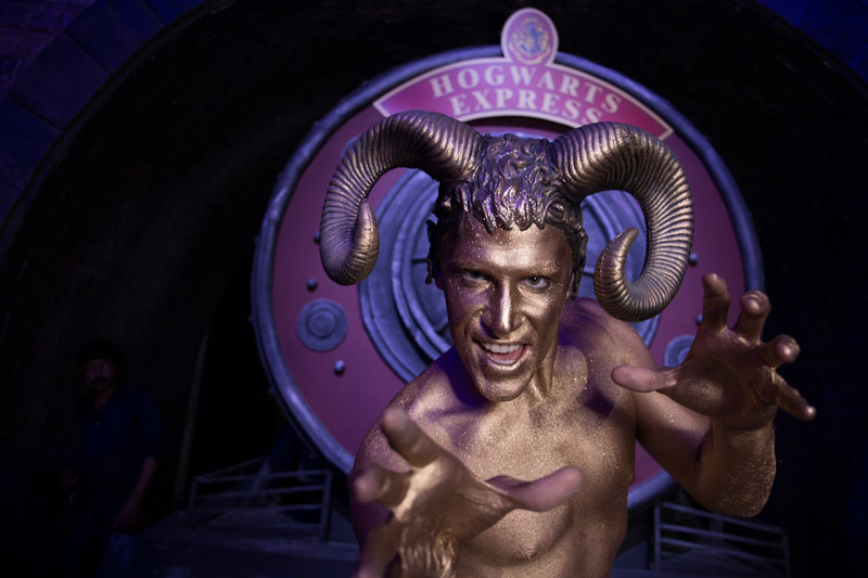 Mann mit goldener Bodypainting-Bemalung und großen Widderhörnern posiert expressiv vor dem Eingang des „Hogwarts Express“.