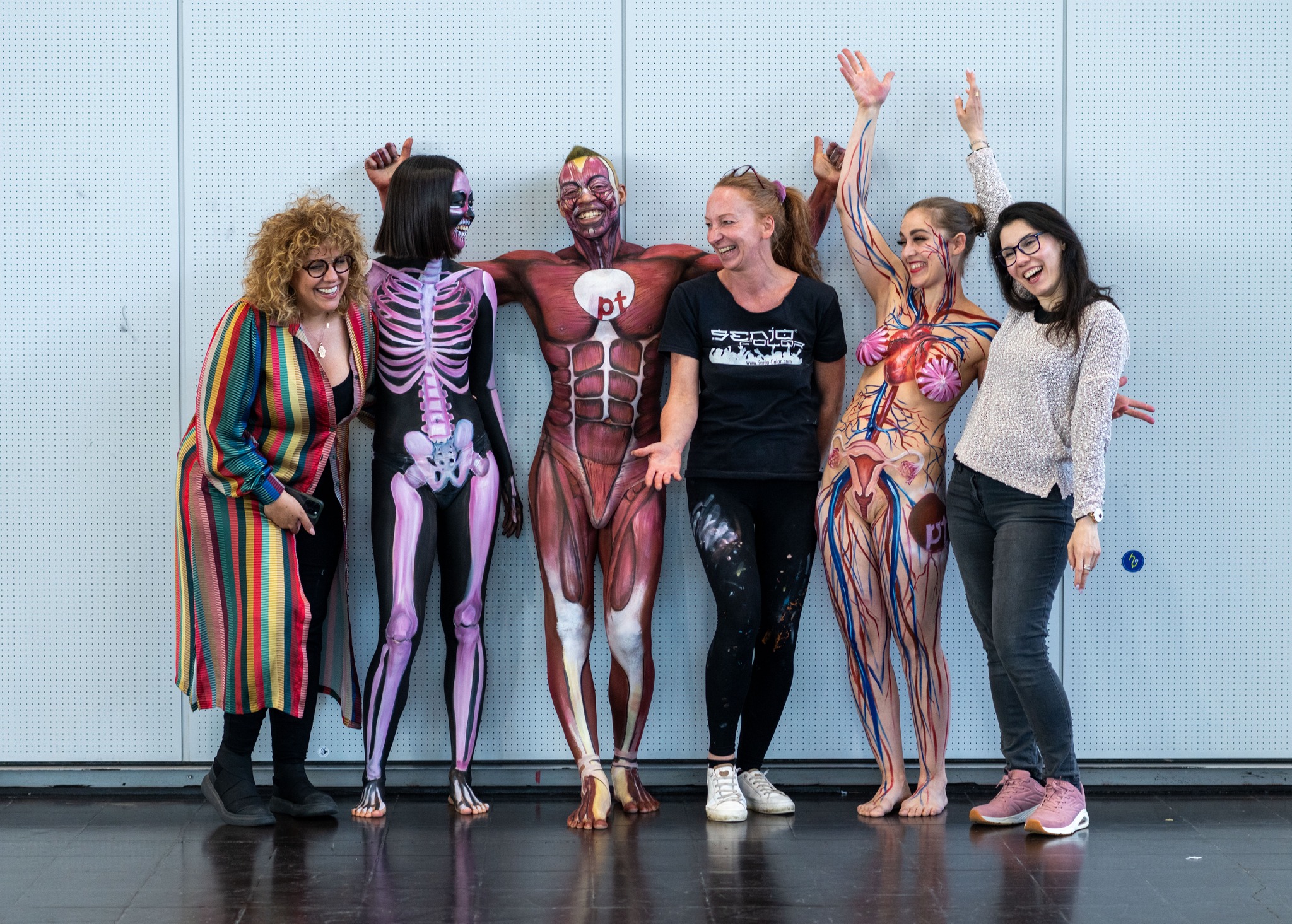 Frau in Leoparden-Bodypainting und großem, mit Früchten geschmücktem Hut posiert am Wasser in der Sonne.