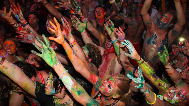 Ausgelassene Partyszene: Eine große Menschenmenge feiert und streckt die bunt mit Farbe bemalten Hände und Körper in die Luft